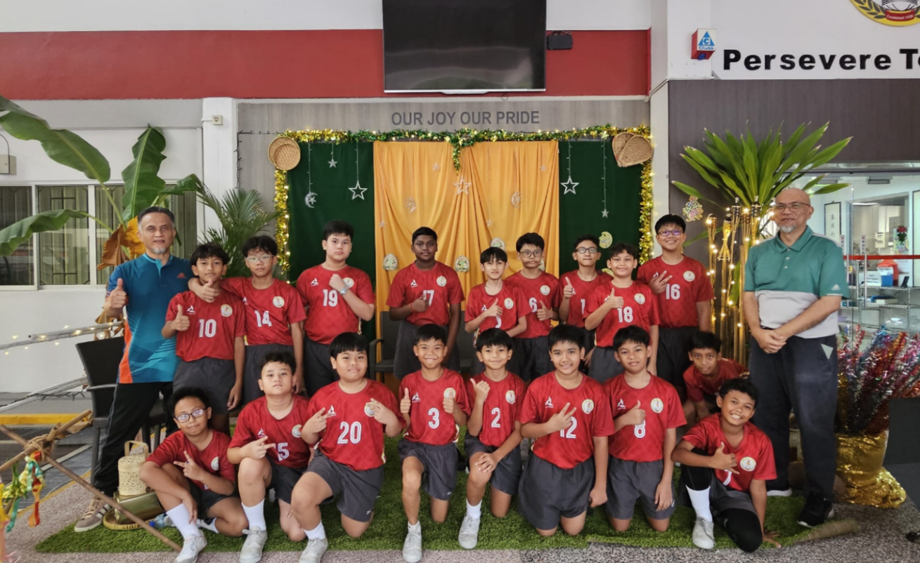 Sepak takraw students dressed in their red jerseys and black shorts posed together with their instructor and teacher in charge outside General Office